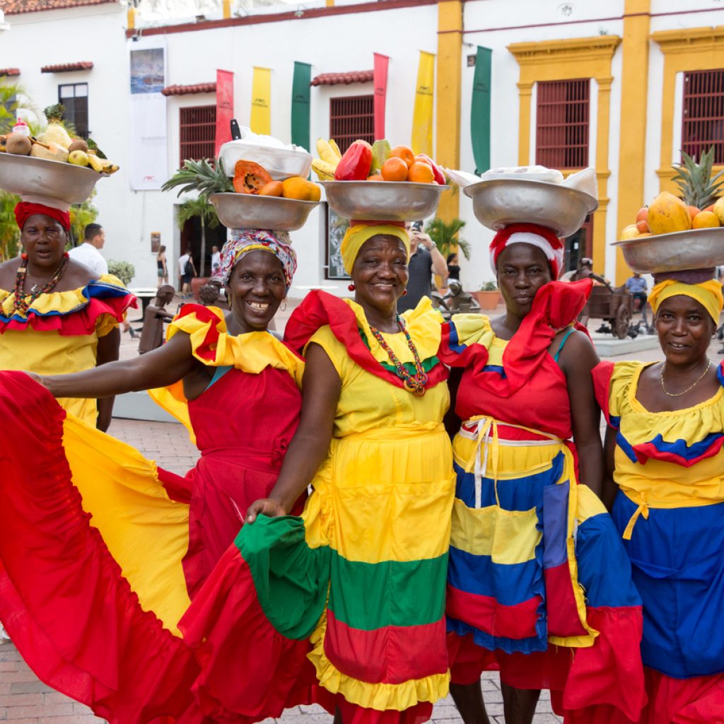 Cartagena: Five palenqueras with a metal basket with fruits are posing showing their multicolor traditional dress at the old town of Cartagena de Indias.