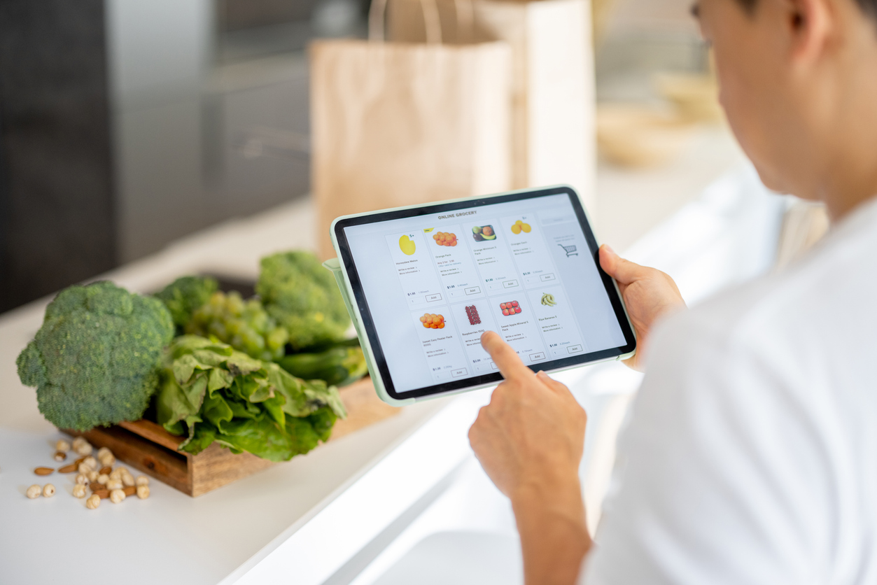 Man searching for produce deals online on tablet, with fresh produce in background.